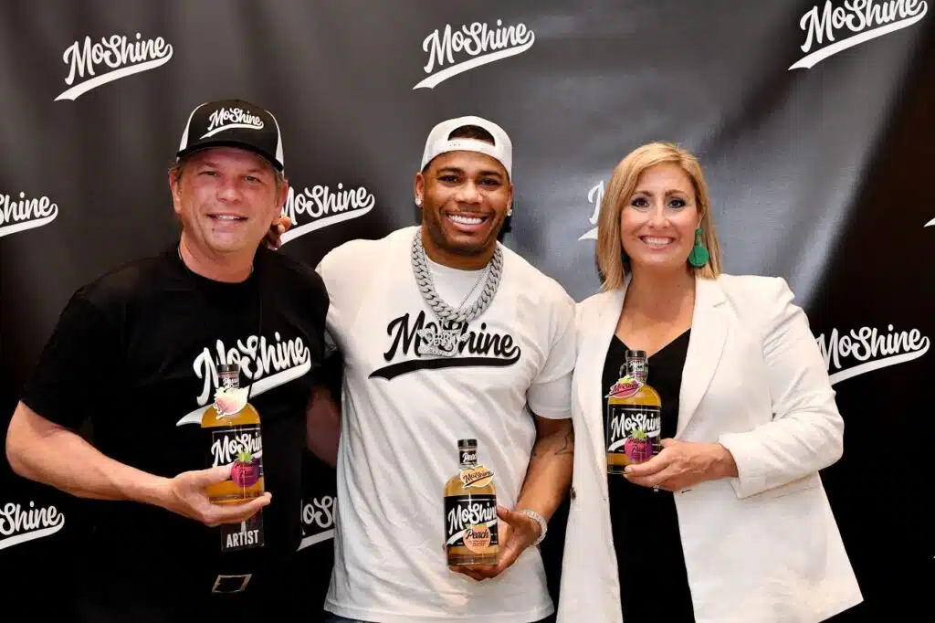 Nelly presenting MoShine moonshine bottles with two executives from Piedmont Distillers 